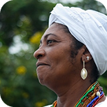 Woman wearing a head wrap outdoors, gently smiling.